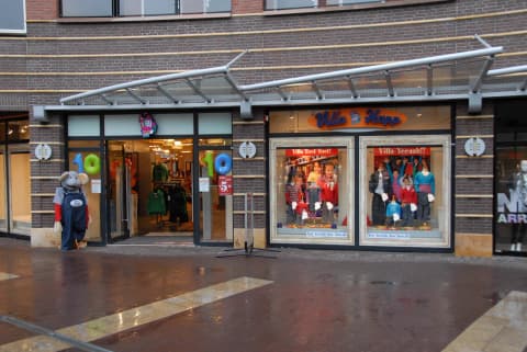 Een Villa Happ winkel met het logo boven de etalages, kinderkleding in de vitrines en Arjo the Rat bij de ingang.